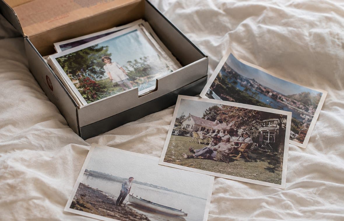 A shoebox of old prints spread out on a bed